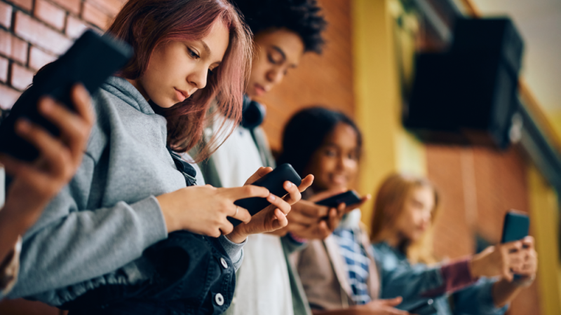 Group of teenagers using mobile phones in hallway at high school.