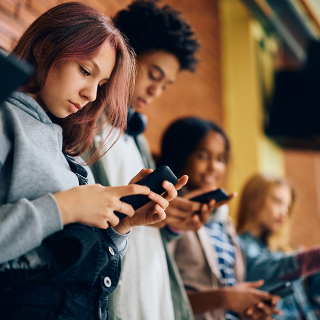 Group of teenagers using mobile phones in hallway at high school.