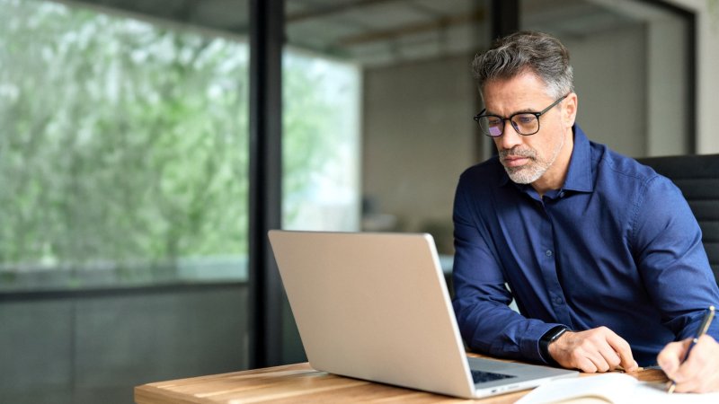 A government affairs professional reviewing notes while working on a laptop at their desk