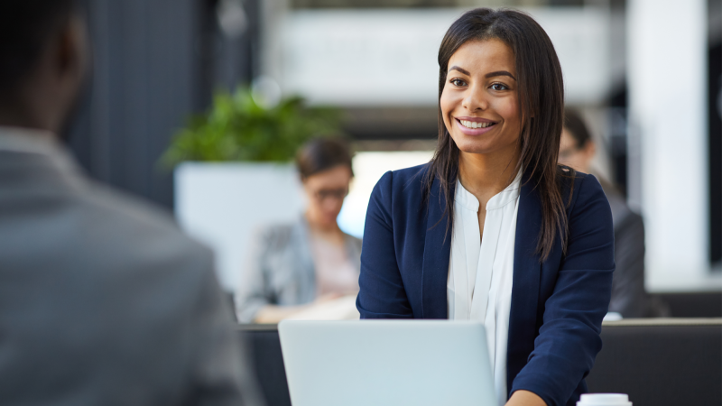 Happy, confident, young woman in a jacket, sitting while holding a meeting in a courtyard.