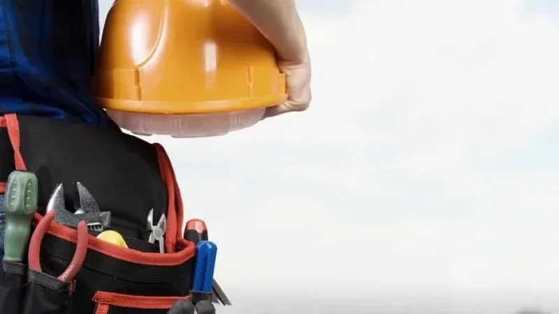 Close up of woman mechanic with yellow helmet in hand against city background